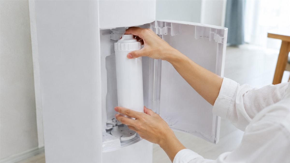 浄水型ウォーターサーバーの前面カバーを開けて白い円筒形のフィルターカートリッジを交換している様子