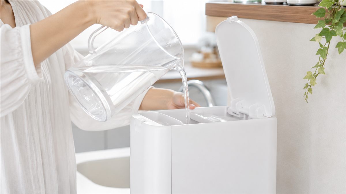 キッチンでピッチャーから浄水型ウォーターサーバーの給水タンクに水道水を注いでいる様子