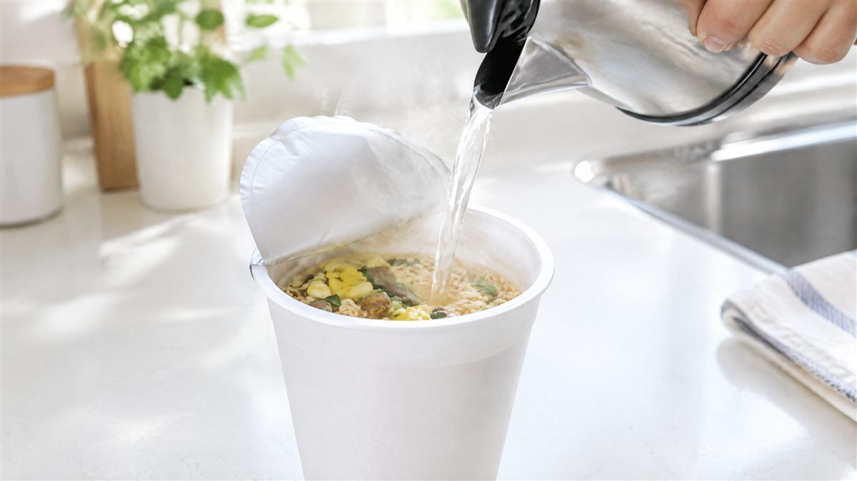 カップ麺の容器にお湯を注いでいる手元のクローズアップ。湯気が立っている様子
